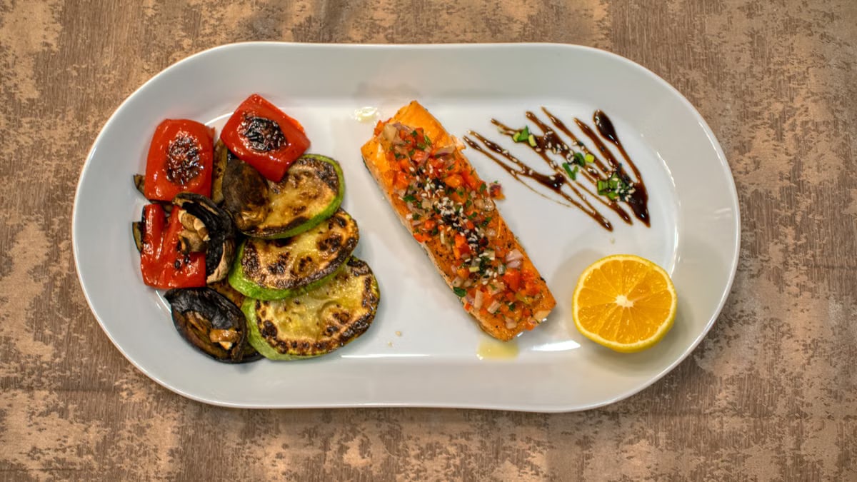 Gourmet grilled salmon served with roasted vegetables and lemon slice on a white plate.